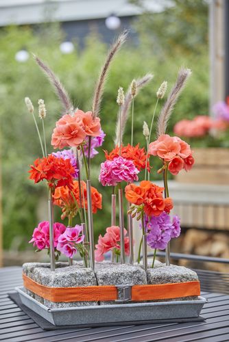 DIY table arrangement with cobbles, metal drinking straws, grasses and colourful geraniums as cut flowers