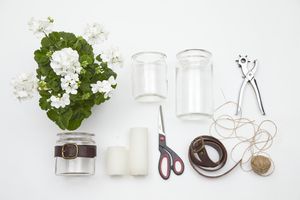 Materialien für DIY Windlichter sind eine Geranie, ein Gürtel, leere Konservengläser, Kerzen, eine Schere, eine Nadel, Zwirn und eine Lochzange.
