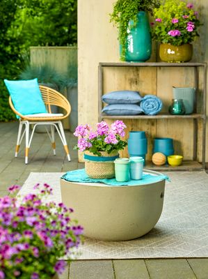 Outdoor living on a terrace with furniture, a rug, purple geraniums, cushions and accessories in yellow and turquoise