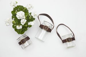 Three upcycled jars with belt buckles and leather handles next to a white geranium