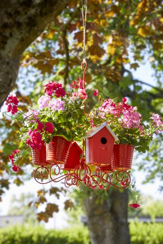 Chandelier with birdhouse and geraniums in pale and bright pink hanging from a tree in a garden