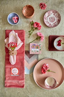 [Translate to Swedish:] Blossoms of pink, red and red-white geraniums with napkins, plates, bowls and cup on table
