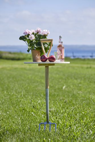 Seegrundstück mit DIY Upcycling Stehtisch aus einer Forke, auf dem eine Geranie im Terrakottatopf, Äpfel, ein Glas und eine Flasche stehen.